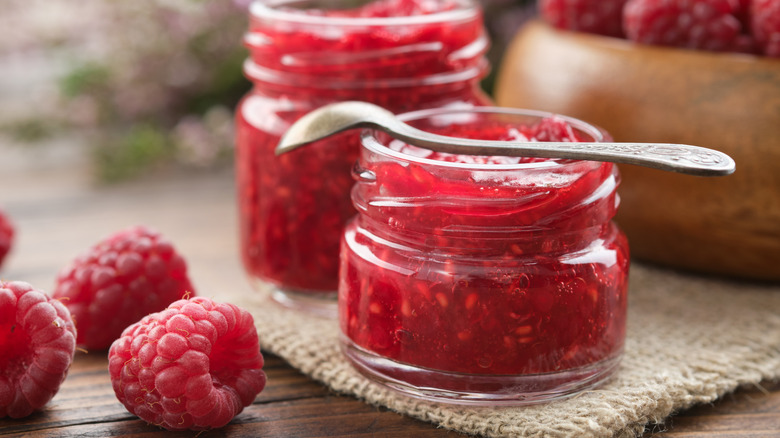 Two small jars of raspberry jam with raspberries alongside