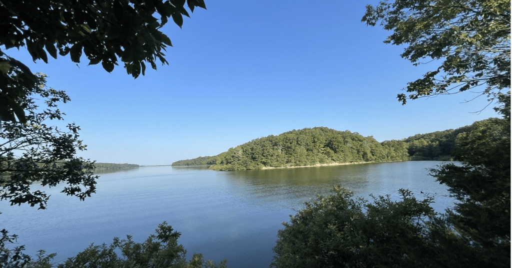Scenic view of Fellows Lake in Springfield, Missouri, framed by lush green trees and a clear blue sky.