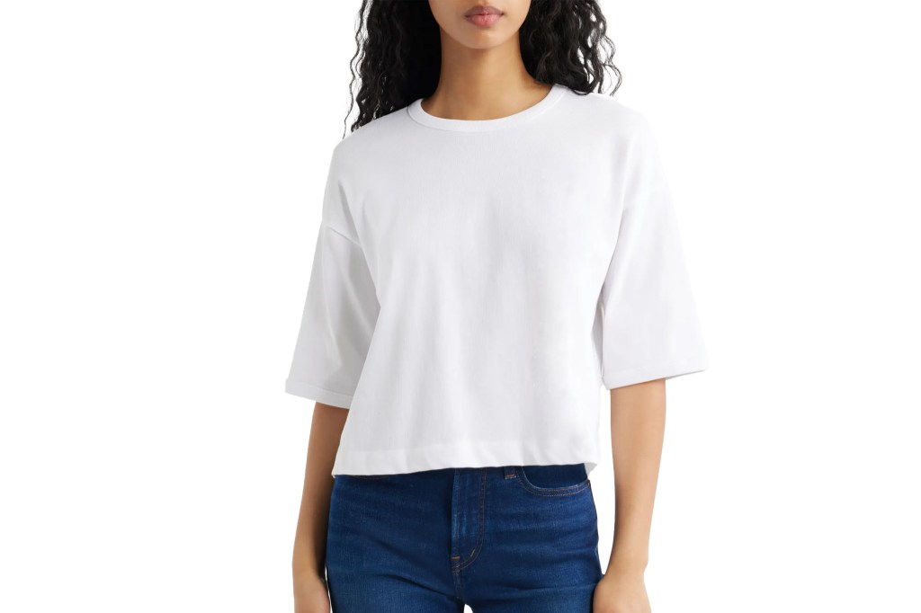 A person with long, dark, curly hair wearing a white tee and blue jeans.