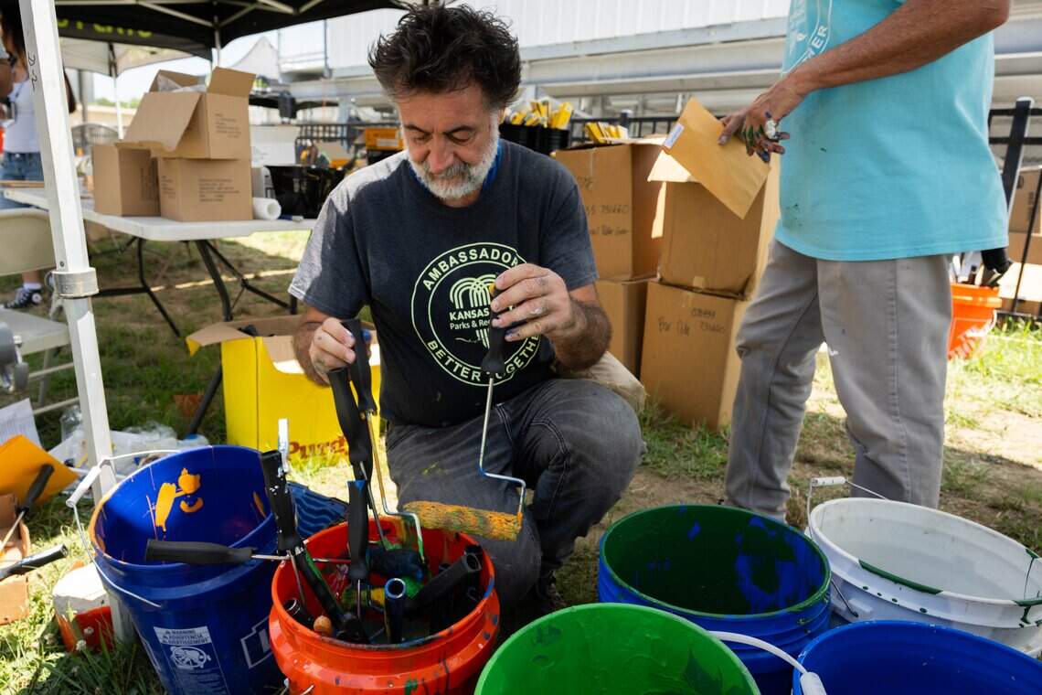 Jean Pasqualini washes brushes and paint rollers for artists on Van Brunt Boulevard in Kansas City, on Monday, July 20, 2026. Volunteers gathered to paint a series of murals featuring more than 100 flags representing the demographics of the neighborhood.