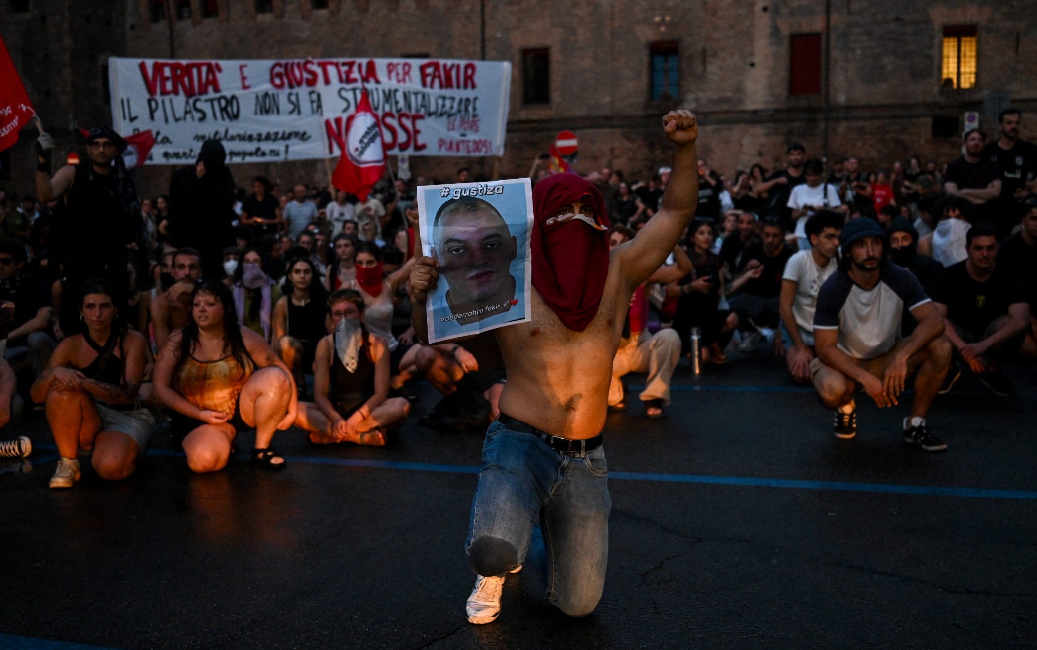A protester kneels, raises a fist and holds a portrait of Abderrahim Fakir