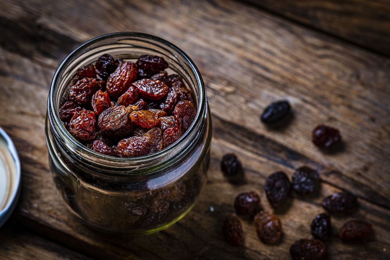 A jar filled with dried fruits on a wooden surface some scattered outside the jar
