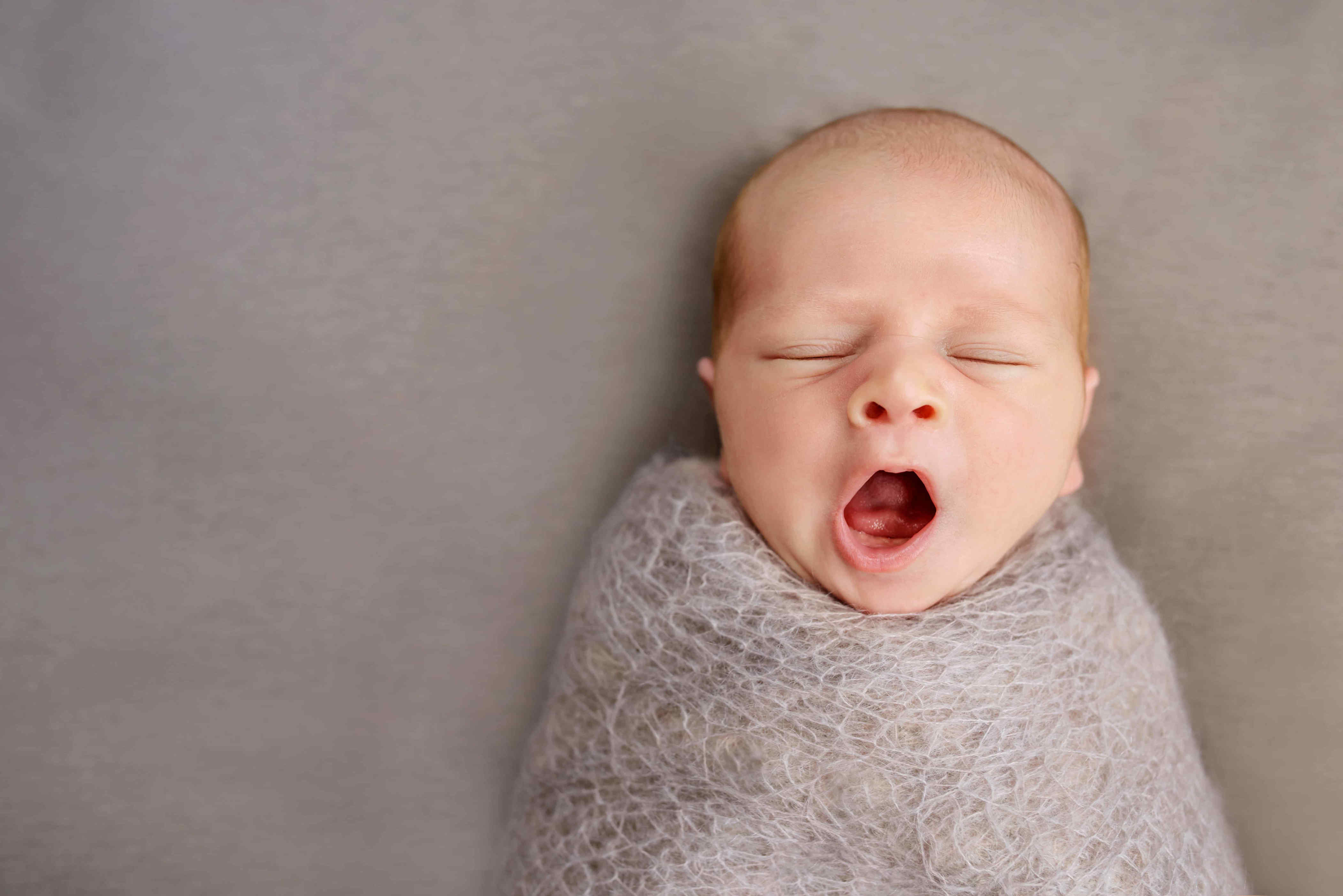 yawning baby swaddled with eyes closed