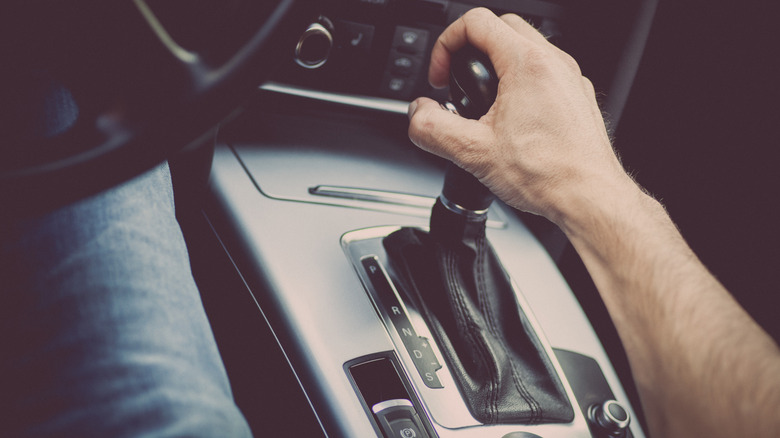 A hand pulling an automatic gear shifter in a new car.