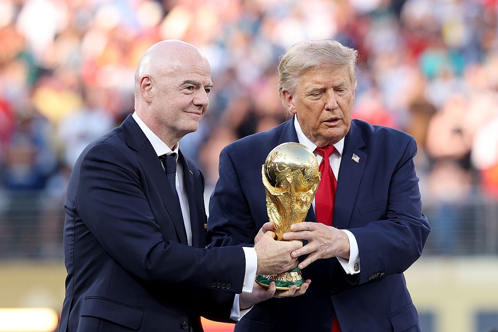 Two men in suits are holding a golden trophy together at what appears to be a formal event
