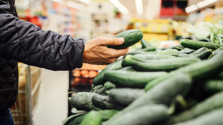 Hand picking up cucumber at grocery store