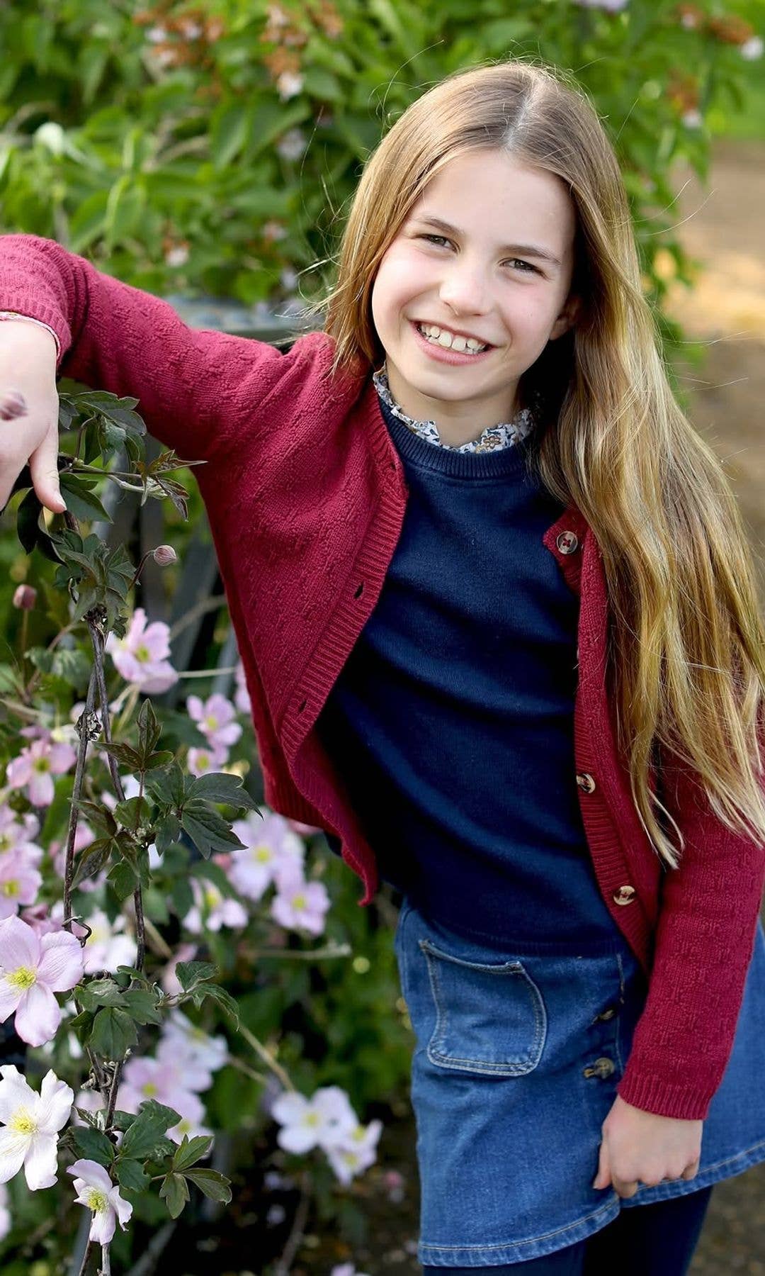 Princess Charlotte leaning against a fence in a red jujmper