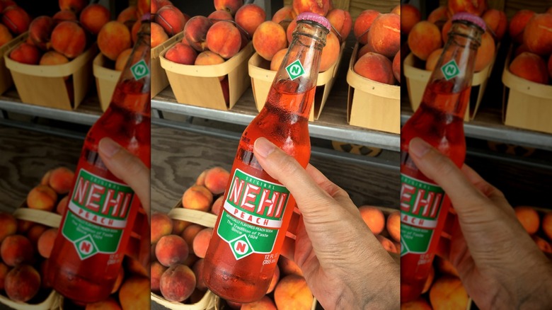 Hand holding a glass bottle of Nehi Peach soda with fresh peaches in the background