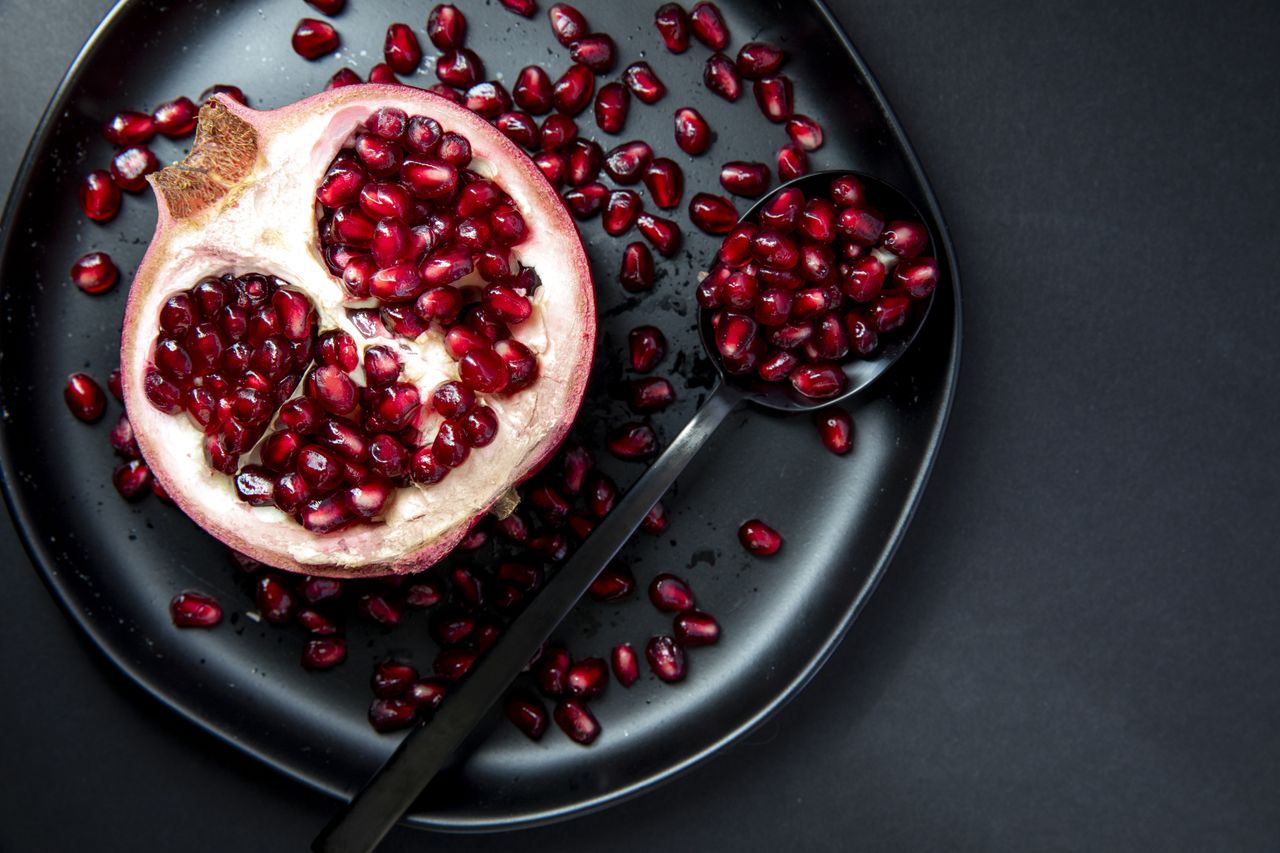 A halved pomegranate and a spoon with seeds on a plate