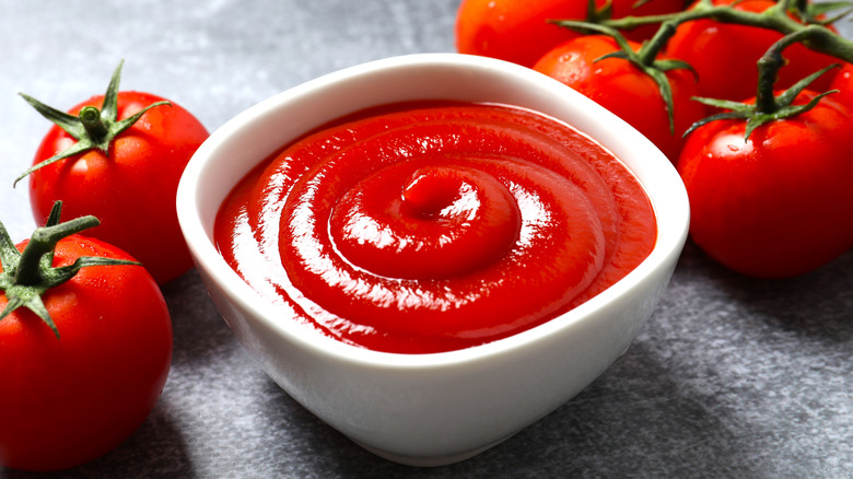 A small bowl of ketchup surrounded by tomatoes