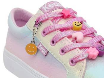 Close-up of a sneaker with pink laces, adorned with emoji charms. A smiley face charm hangs from the lace, offering a playful touch