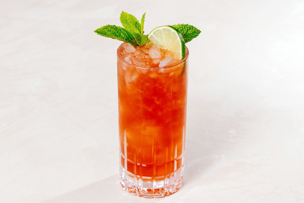Cobra's Fang cocktail, bright red, in a highball glass with crushed ice, a mint spring and lime wheel for garnish