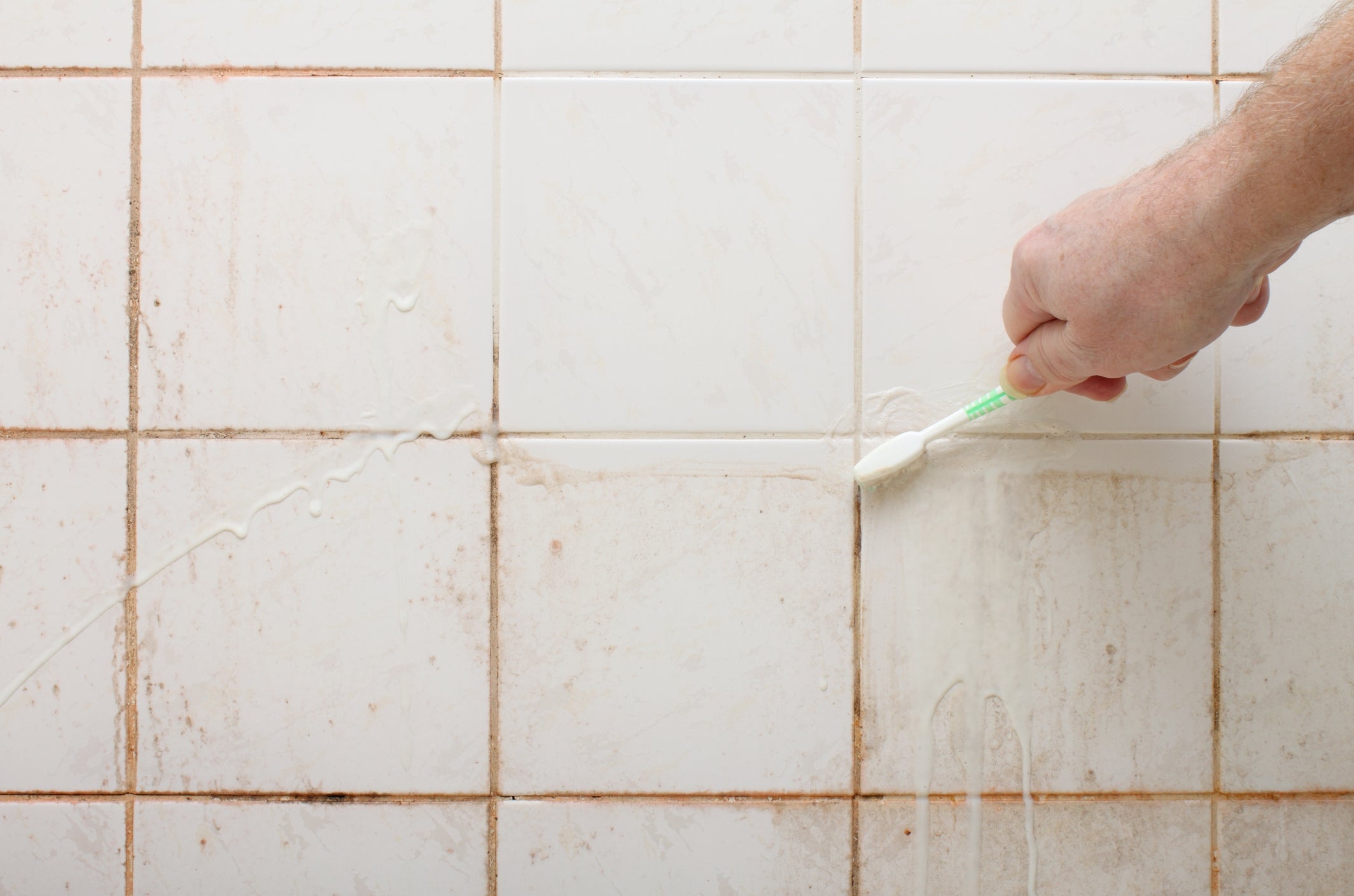 Hand scrubbing tile grout with a toothbrush to clean it, demonstrating a cleaning hack for dirty tiles