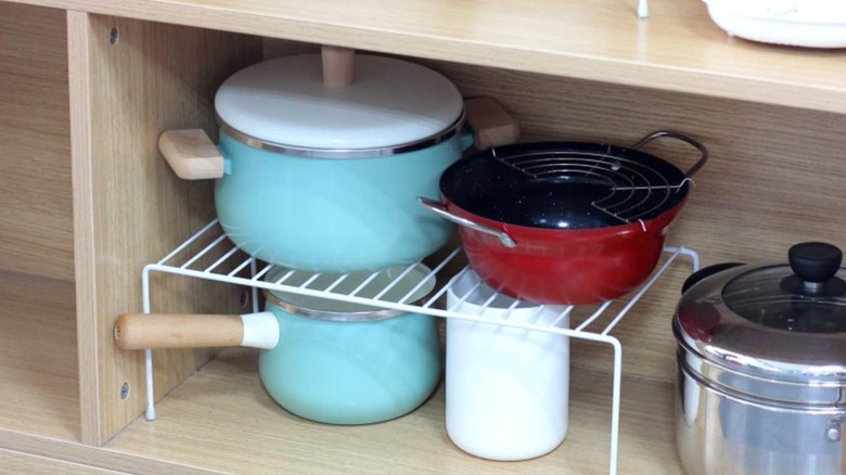 Pots and pans organized in a cabinet with a shelf riser.