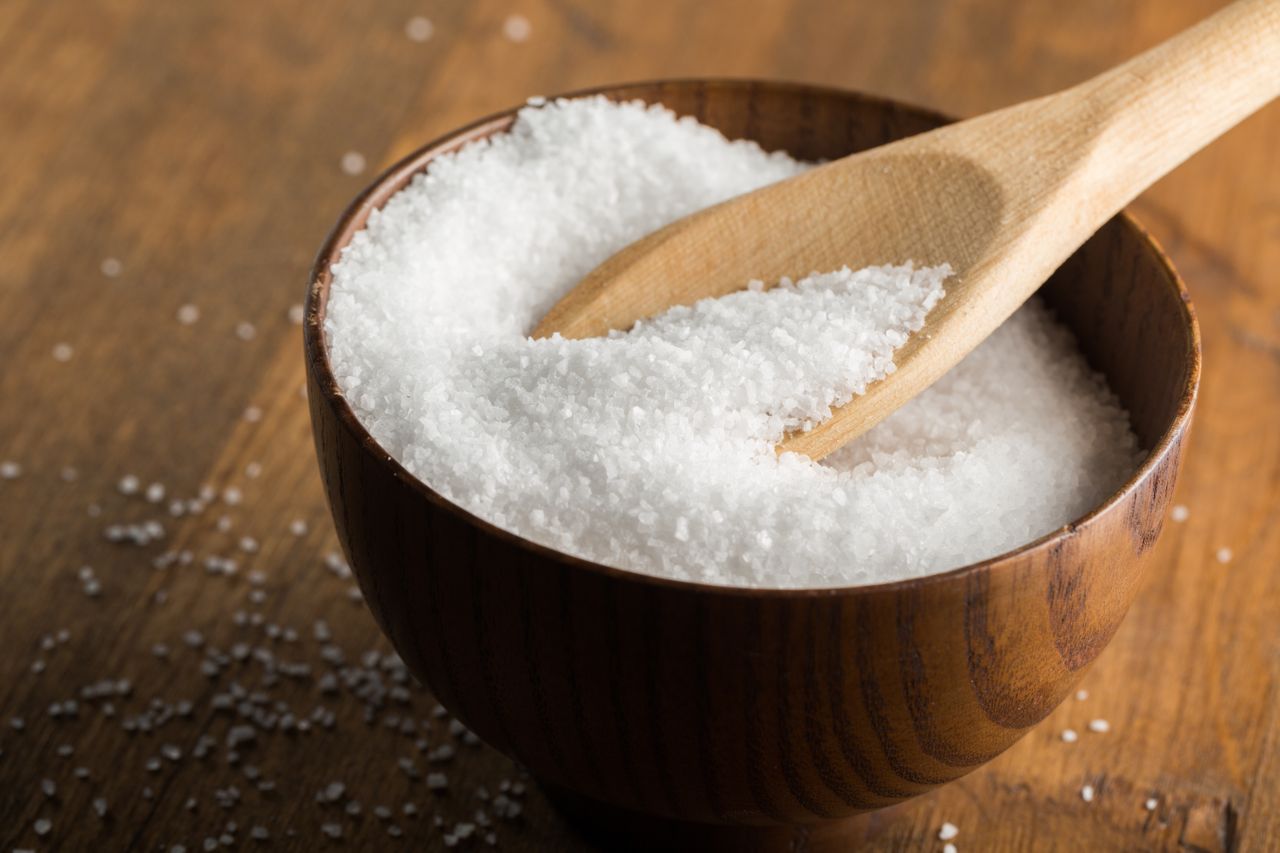 A wooden bowl filled with granulated salt a wooden spoon resting inside the bowl