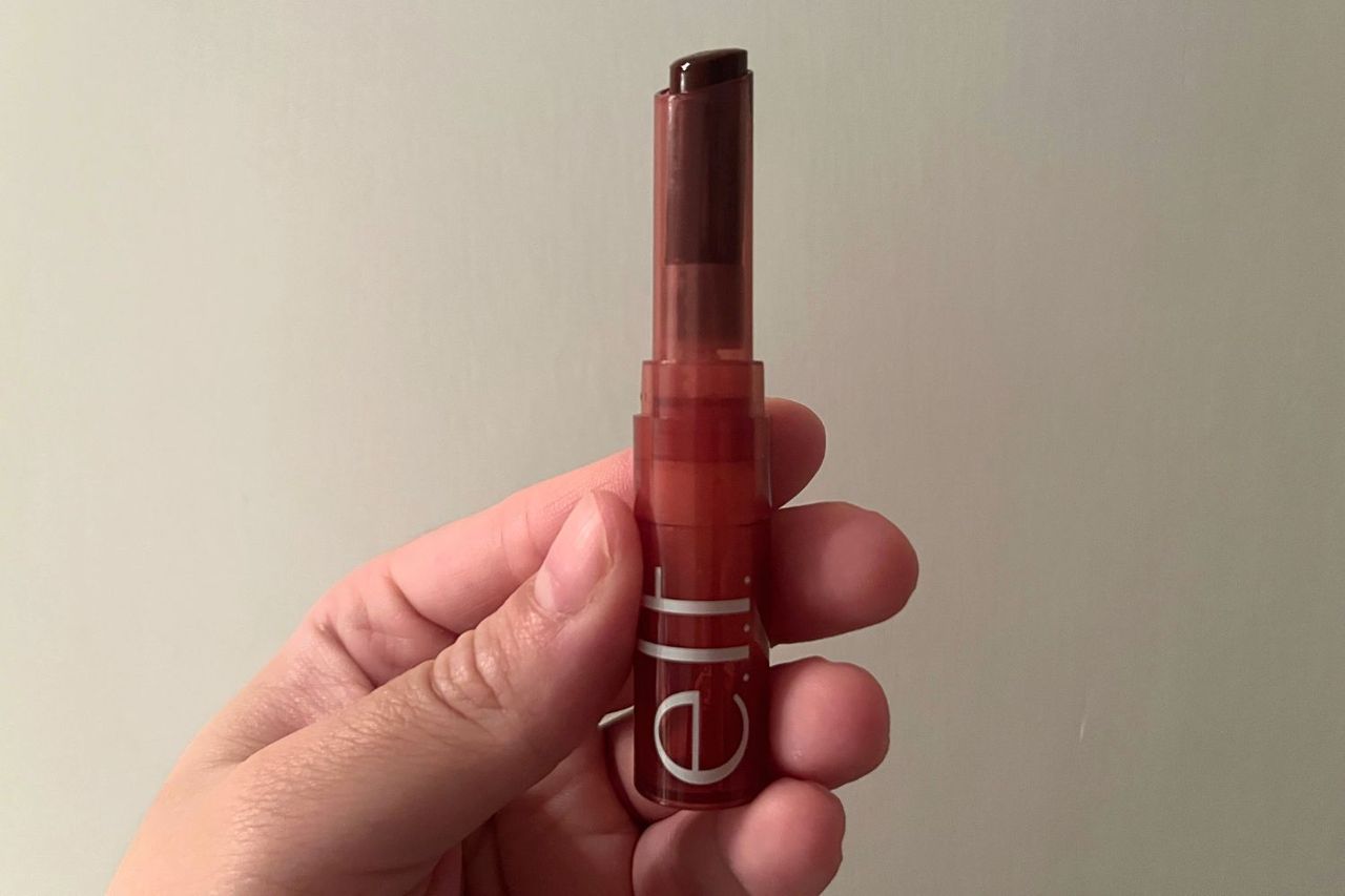 A hand holding an elf lipstick with a sheer blackcherry shade