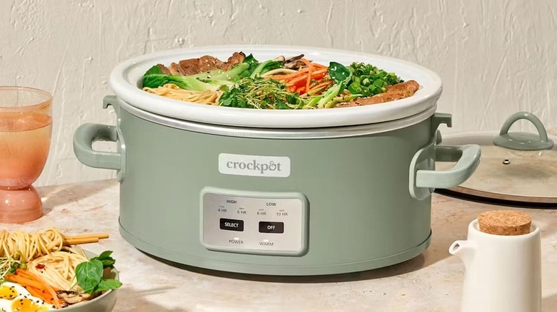 light green slow cooker opened to show a vegetable, chicken and noodle dish