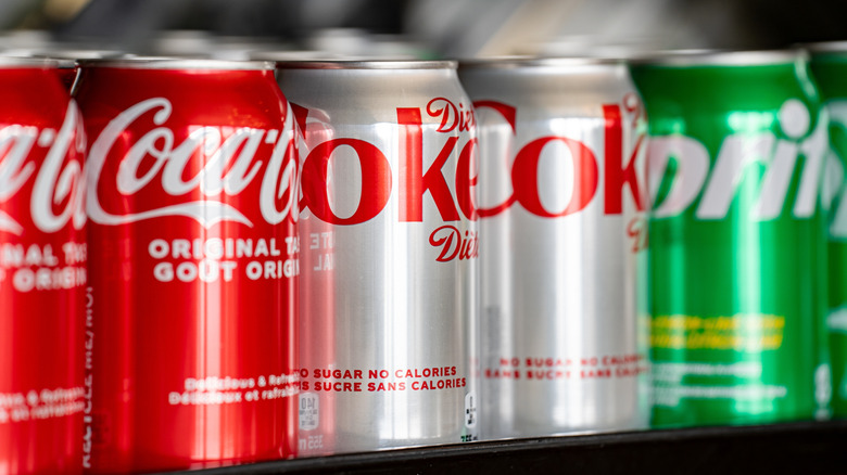 Cans of Coke, Diet Coke, and Sprite lined on a store shelf