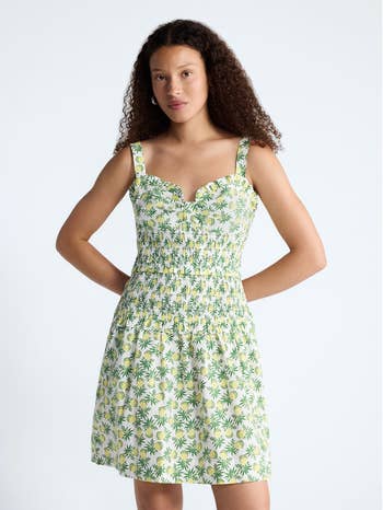 Person wearing a sleeveless floral-patterned summer dress with a smocked waist, posing against a plain background