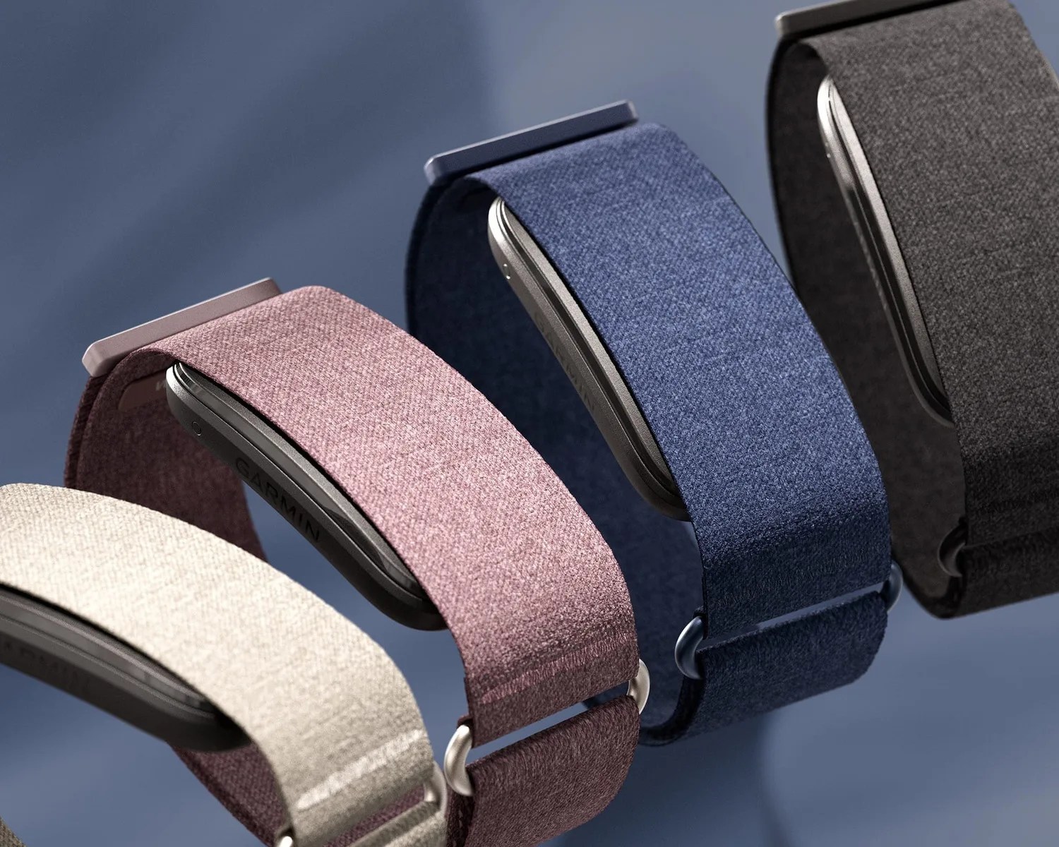 Four smartwatches with fabric bands in beige, mauve, blue, and black on a blue surface.
