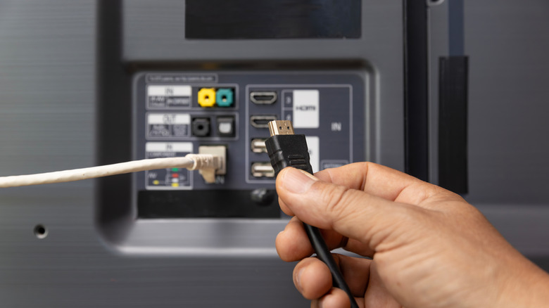 A hand connecting a cable to the back of a TV.