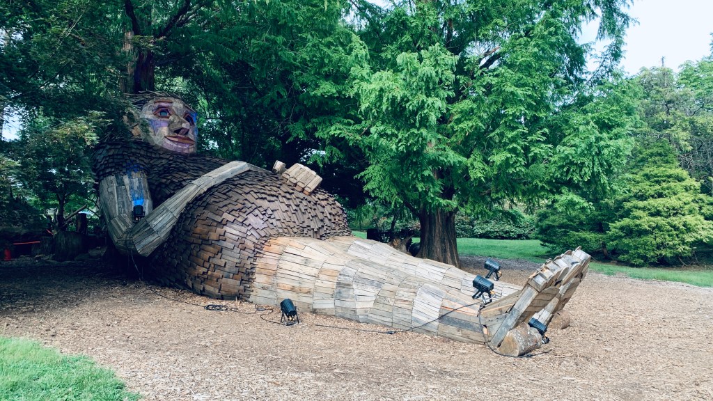 A tall giant troll relaxes under the canopy of some tall trees.