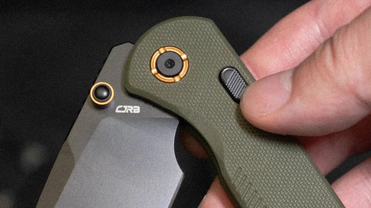 Close-up of a hand holding an olive green folding knife with a black blade marked 