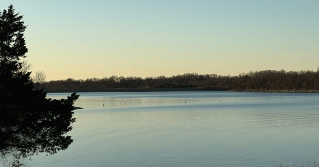 Calm water at Fellows Lake in Missouri during a serene early morning sunrise with tree silhouettes.