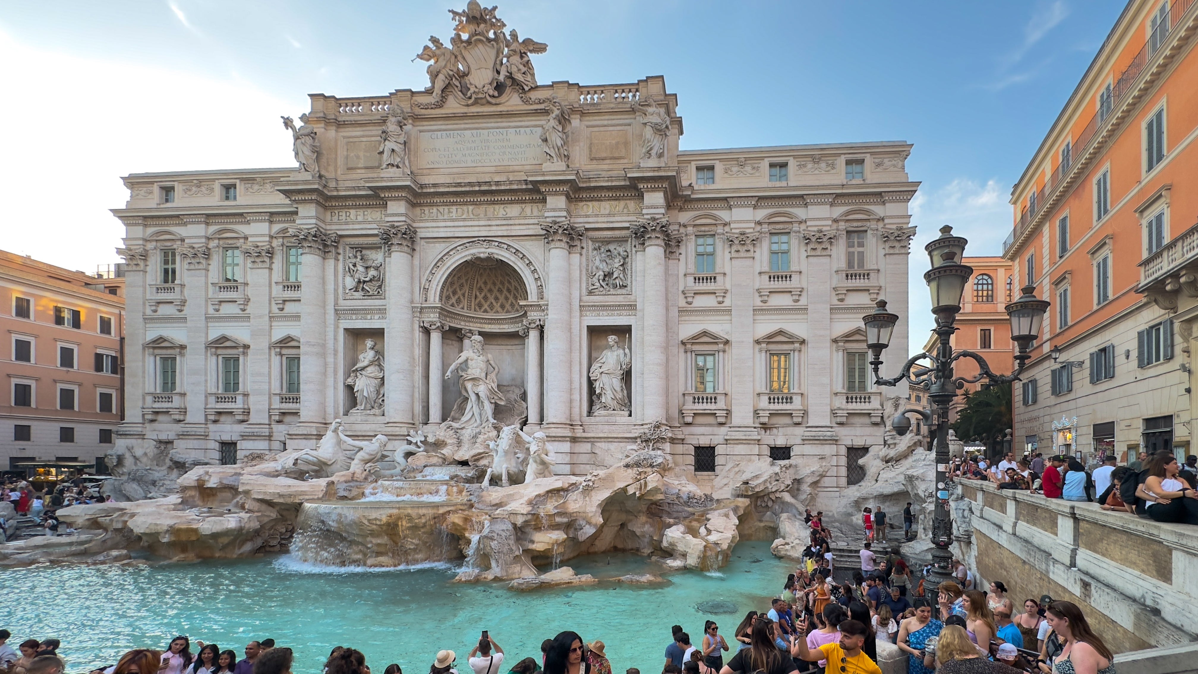 Crowds gather at the historic Trevi Fountain in Rome, admiring the grand Baroque architecture and sculptures