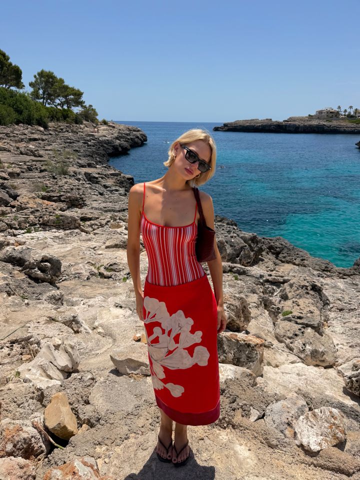 A person in a summer dress standing on rocky terrain near a blue ocean view