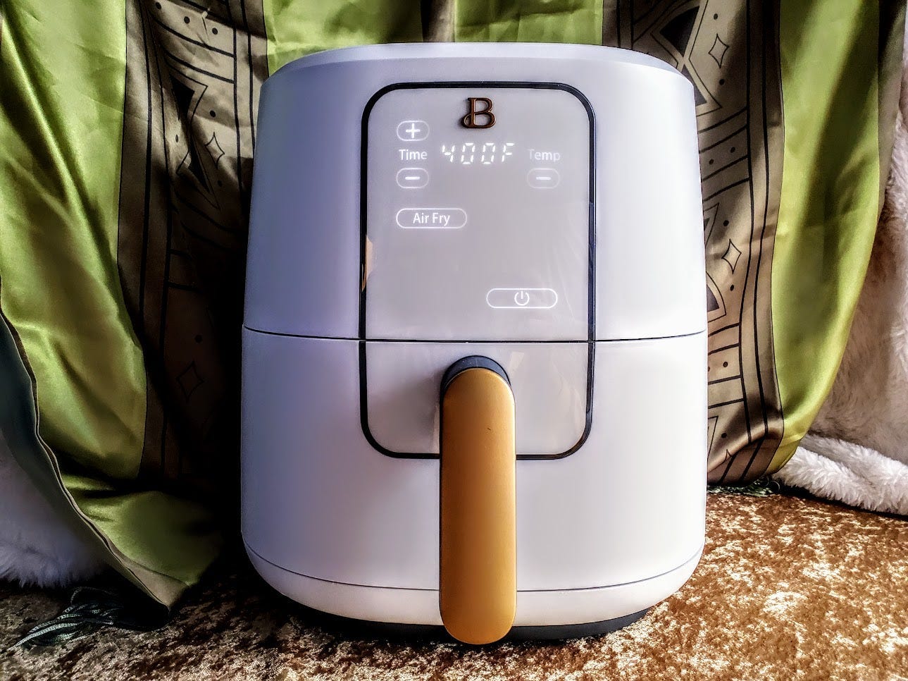 The Beautiful 6 Quart Touchscreen Air Fryer by Drew Barrymore is displayed with a green and gold background.