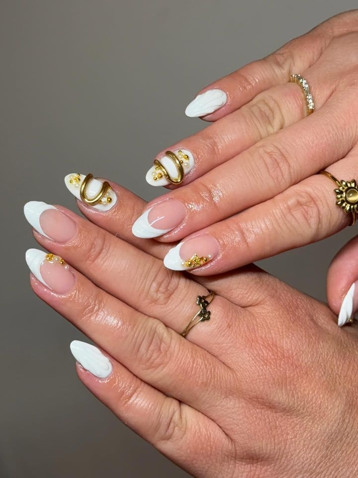 Hands with manicured nails featuring white tips and gold decorative elements