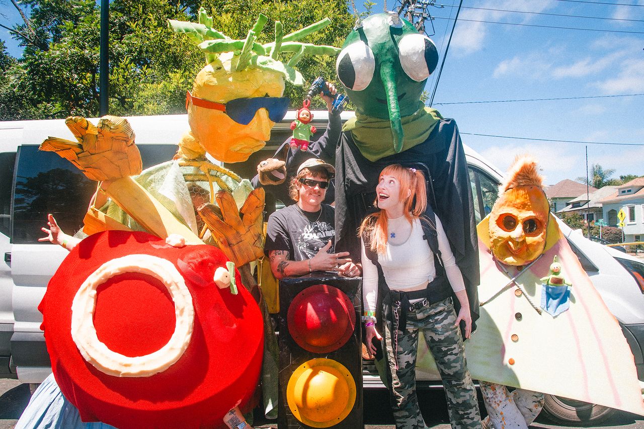 Two people posed in a group with individuals wearing oversized character costumes and props outside in a street environment