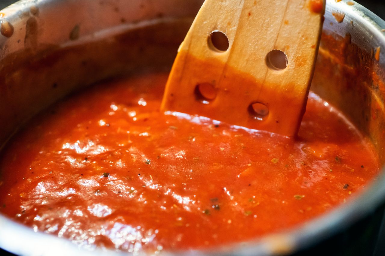 A pot of tomatobased sauce with a wooden spoon resting inside