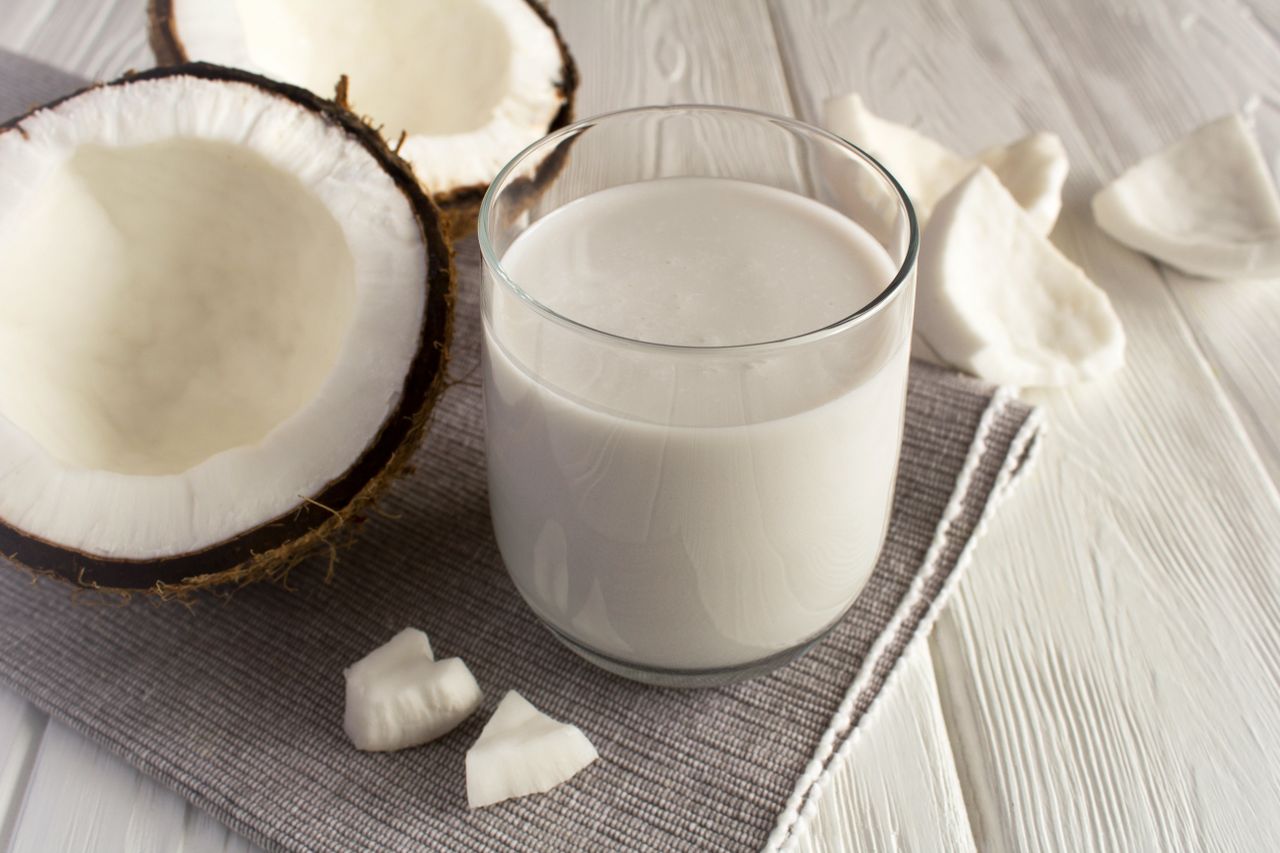 A glass of coconut milk next to a halved coconut and coconut pieces