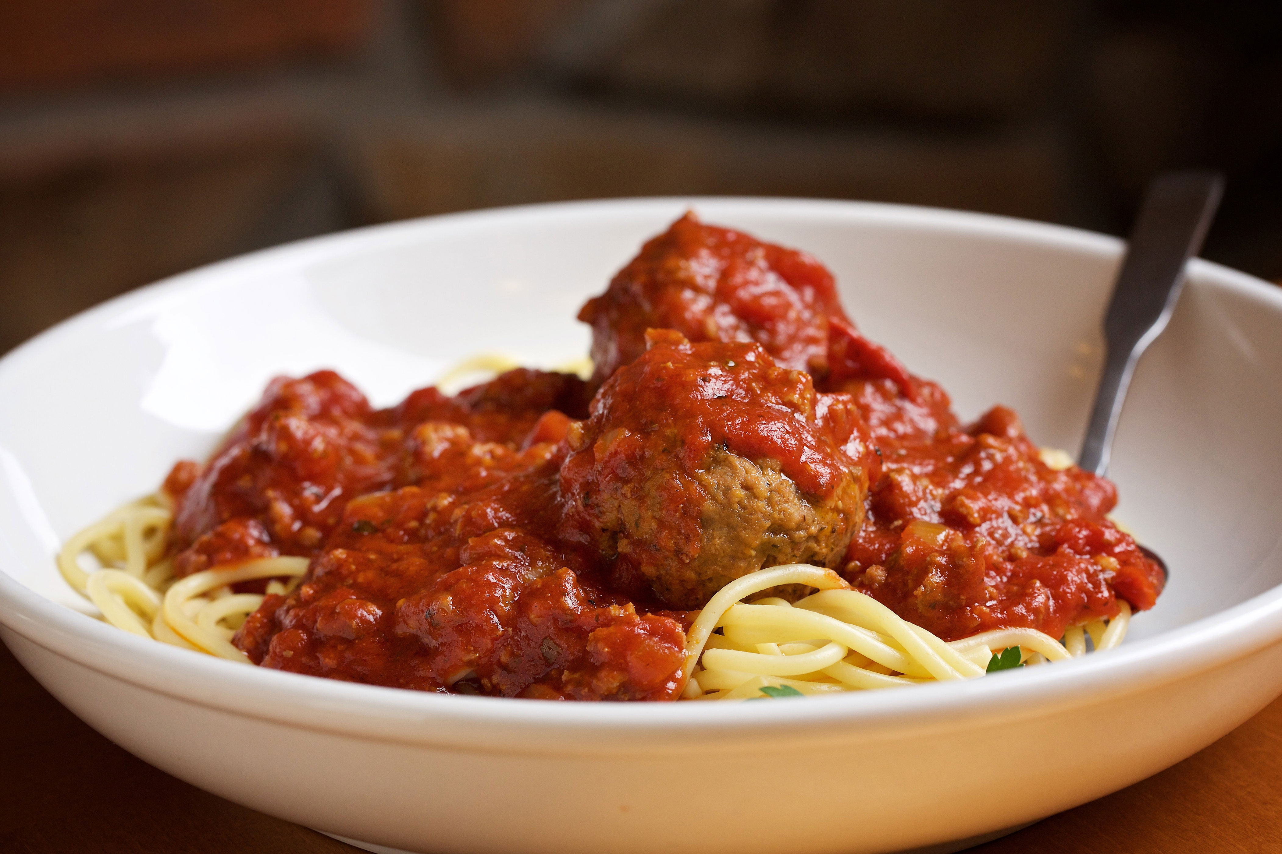 A plate of spaghetti topped with marinara sauce and meatballs, presented with a fork in a white bowl