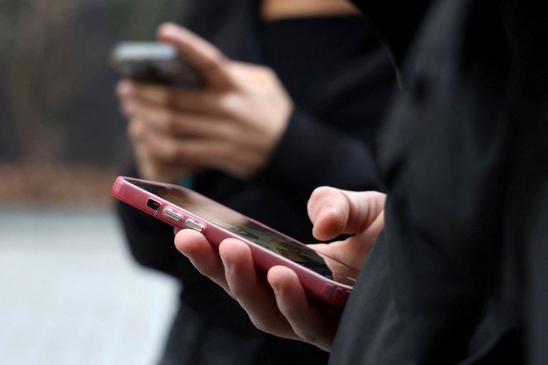 FILE PHOTO: Teenagers look at their mobile phone screens in Paris