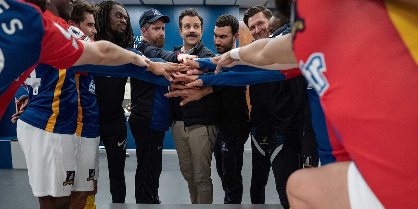The Richmond AFC team in the locker room with hands together in Ted Lasso.