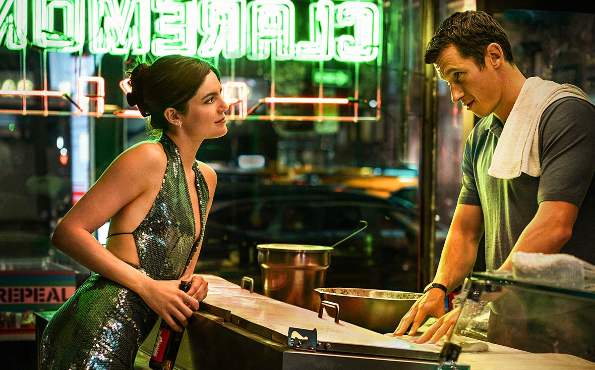 monica barbaro leans over a bar to talk to callum turner in a still from the movie one night only