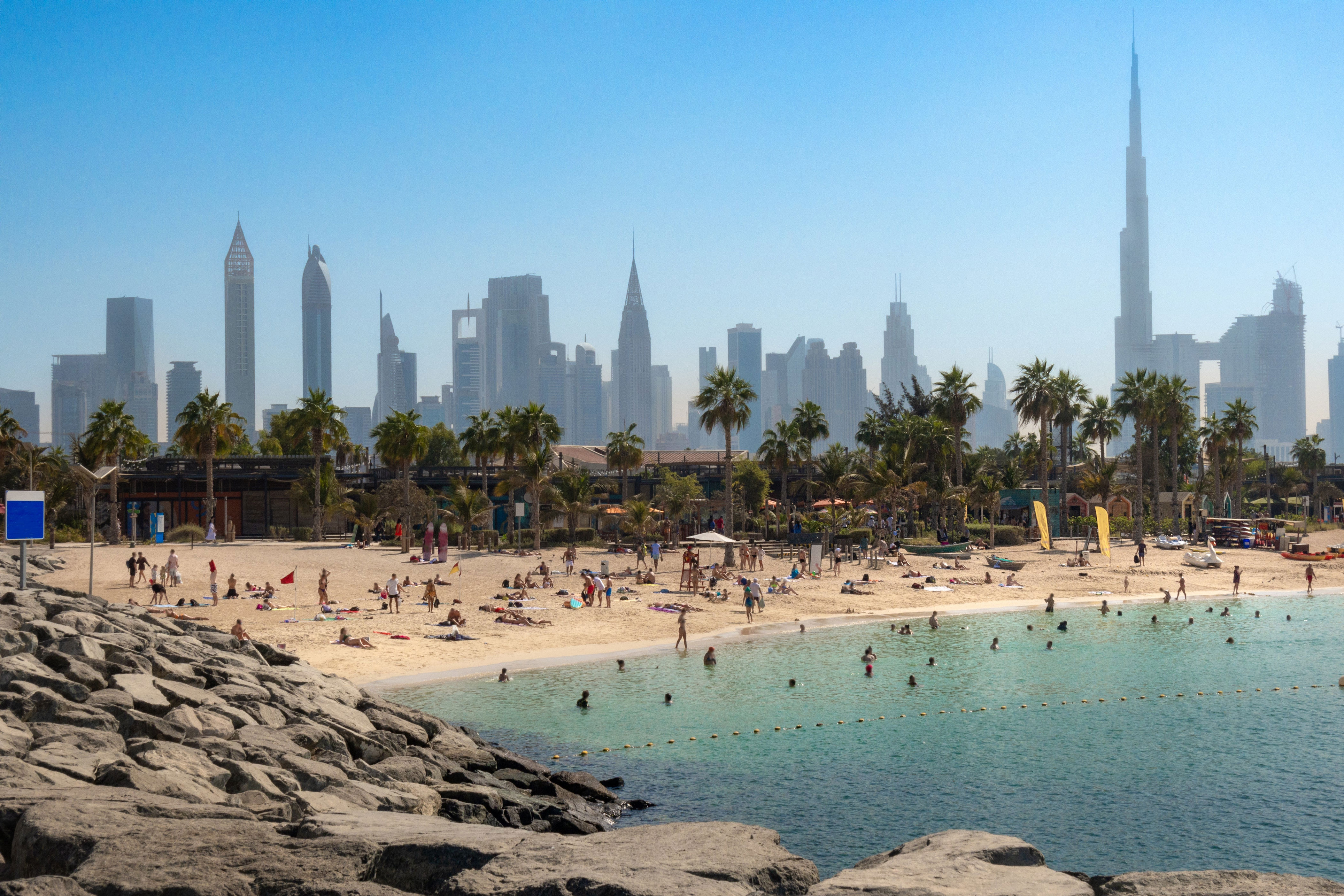 People relax on a sandy beach with a city's skyline in the background, showcasing both natural and urban landscapes