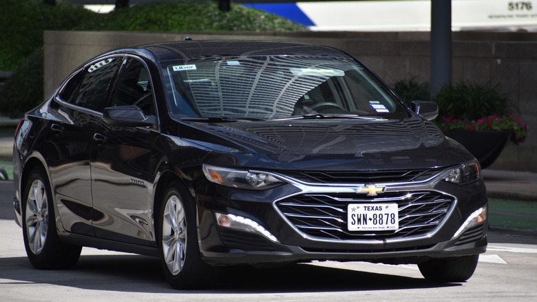 A front shot of a black Chevrolet Malibu with Texas plates, driving