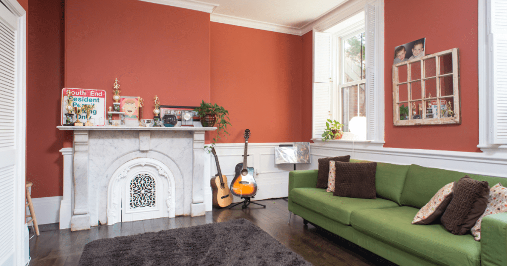 The interior of a historic Airbnb in Boston, Massachusetts, with orange walls, a marble fireplace, a green sofa, and modern decor.