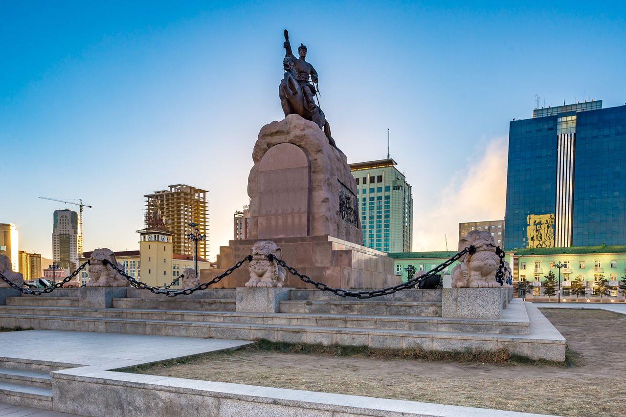 A statue in the center of a square with surrounding modern buildings