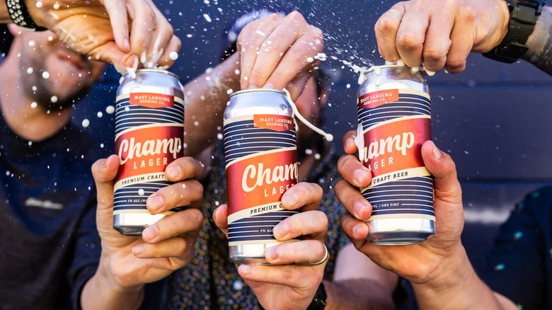 Three hands opening cans of Mast Landing Champ Lager