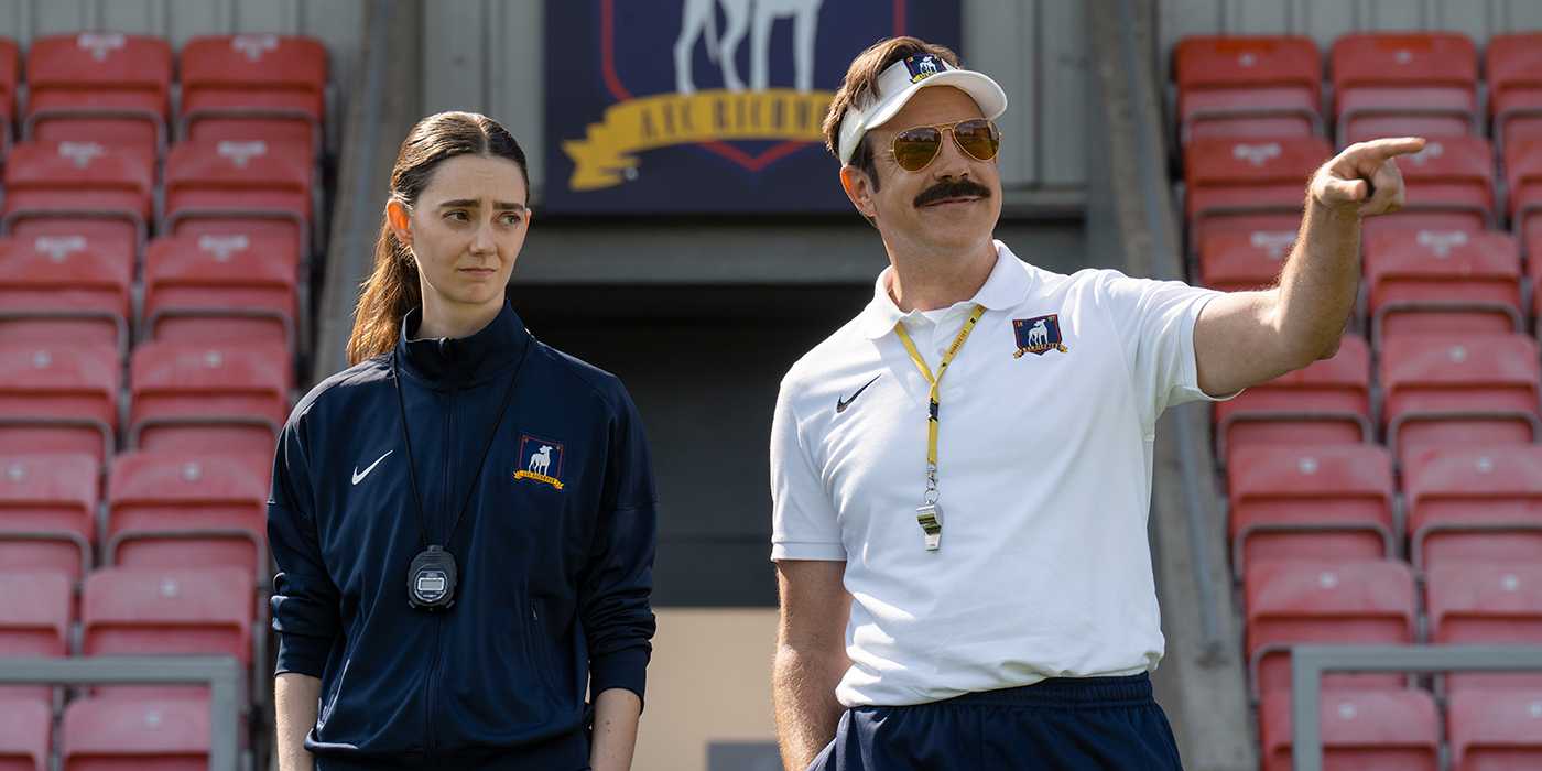 Ted with a female coach standing on the football field in Ted Lasso