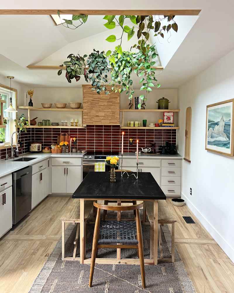 white kitchen with deep red tile backsplash and skylights with lots of plants