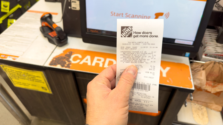 Hand holding a bill near the Home Depot checkout counter