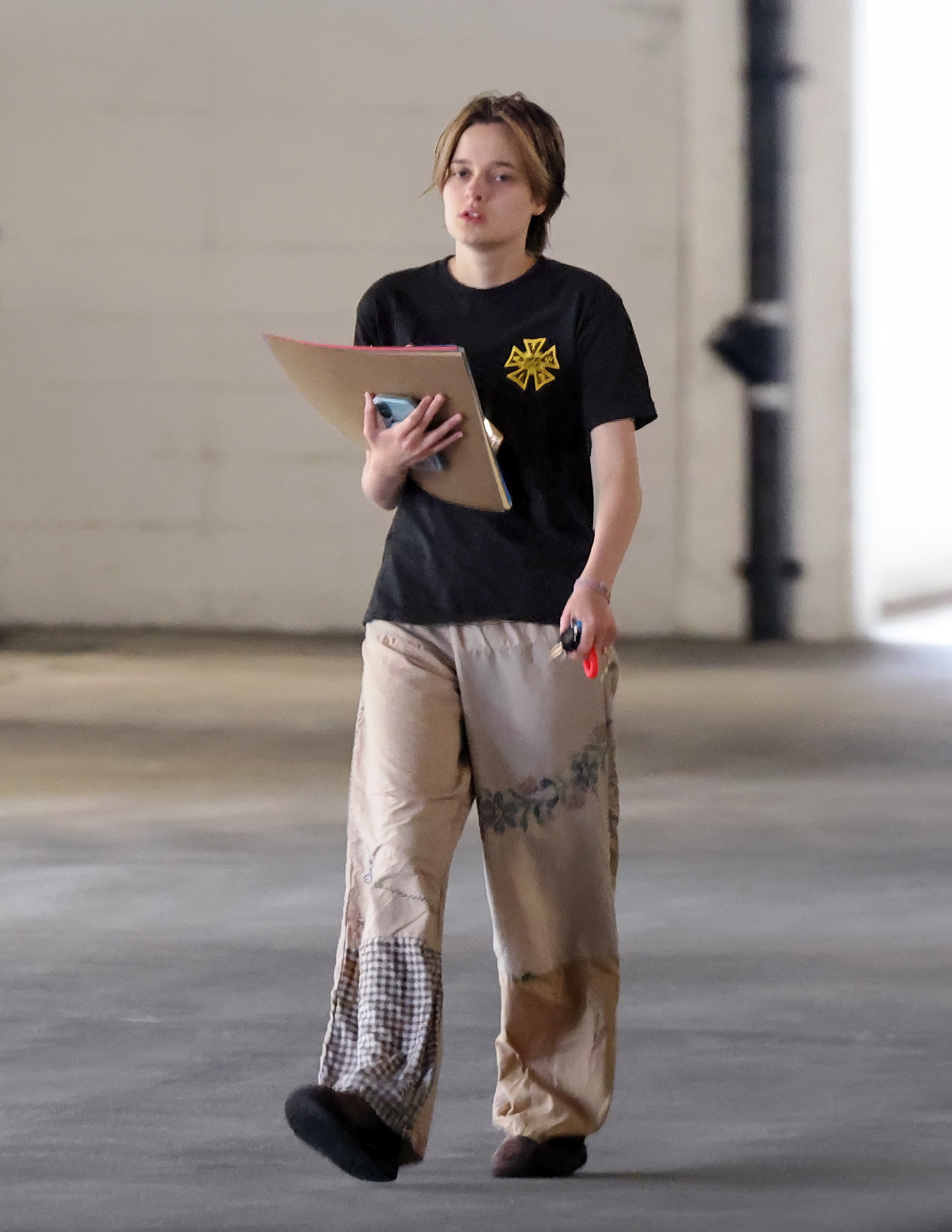 Vivienne Jolie walking in a parking garage holding art supplies.
