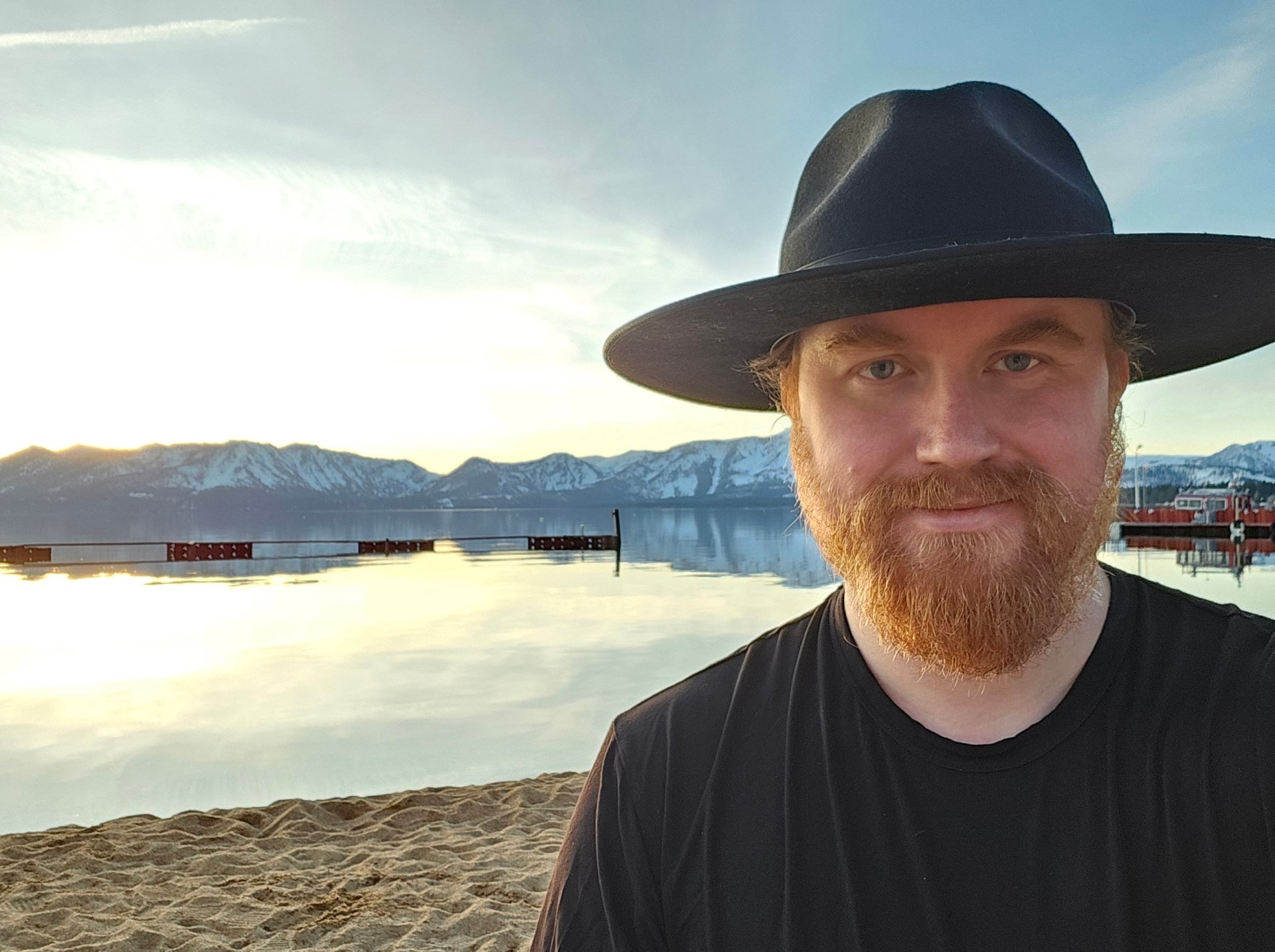 Bjorn, an adul, with a ginger beard and a black hat with a wide rim. He is on a beach and looks directly at thhe camera.