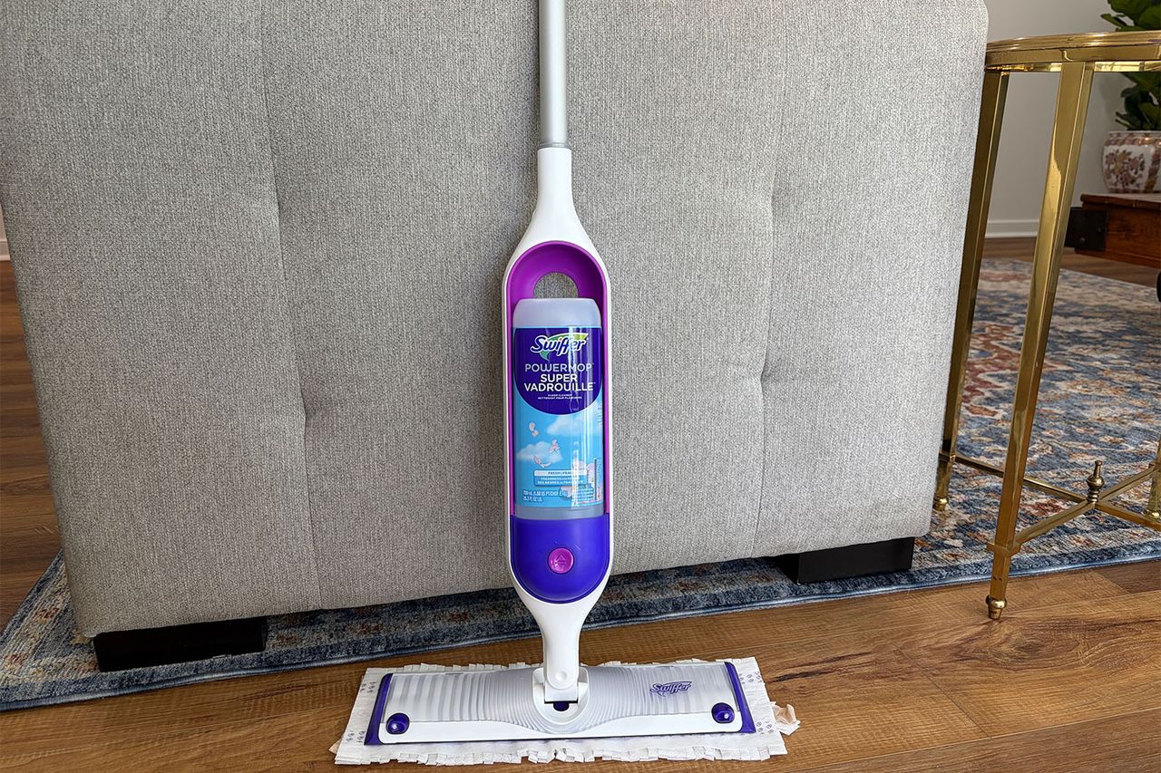 Swiffer Powermop placed upright against a couch on a wooden floor with a rug edge visible